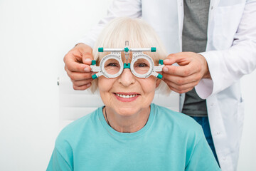 Smiling senior woman wearing optometrist trial frame at ophthalmology clinic. Ophthalmologist...