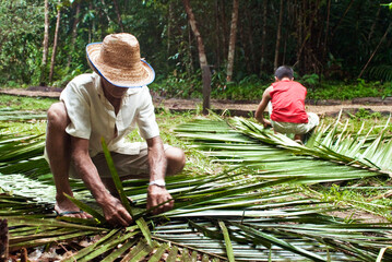 Homens tran&ccedil;ando a folha do Baba&ccedil;u para confec&ccedil;&atilde;o de telhado