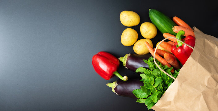 Above View Of Fresh Organic Vegetables Spilling Out Of Paper Shopping Bag On Dark Kitchen Counter, Healthy Eating And Cooking Concept