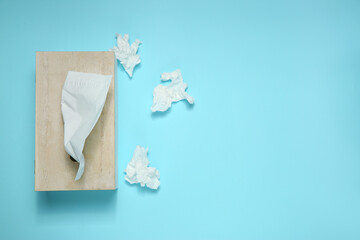 Used paper tissues and wooden holder on light blue background, flat lay. Space for text