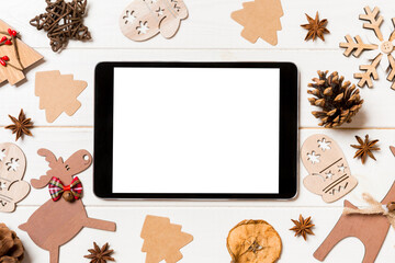 Top view of tablet on holiday wooden background. New Year decorations and toys. Christmas concept