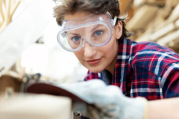 Young beautiful 30-40 professional female carpenter looking grinding raw wood with sandpaper in...