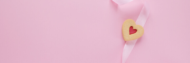 Cookies in the shape of a heart with a pink ribbon on pink background.