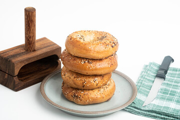 A Single Tall Stack Of Freshly Baked Bagels On A Ceramic Plate With Wood Cutting Stand And Knife
