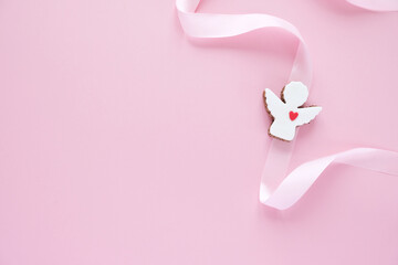 Cookies in the shape of an angel with pink ribbon on pink background.