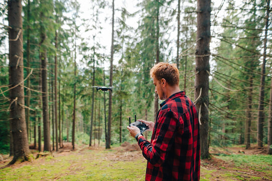 Handsome young man controls a drone in the woods, looking intently at the remote control. Drone flights and video shooting in the untouched forest.