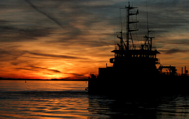 Silhouette image of fishing boat lighted by sunset