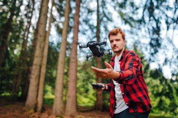 Young man stands in the woods and launches a drone into the air with his hands. Focus on the drone...