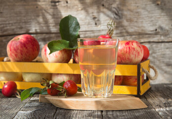 A glass of apple juice and fresh apple on a wooden background in the sunlight.