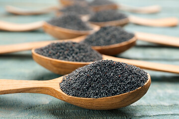 Poppy seeds in spoons on blue wooden table, closeup
