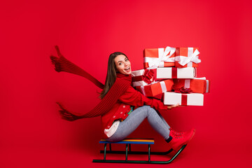 Full length body size profile side view of her she attractive glad cheerful girl riding sledge having fun delivering giftboxes Eve Noel isolated bright vivid shine vibrant red color background