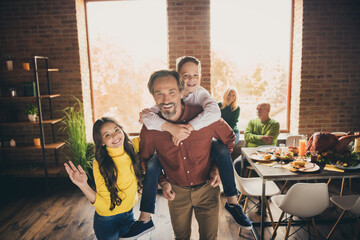 Fototapeta na wymiar Photo of full family gathering five people two small kids play dad piggyback daughter wave hand greeting grandparents sit sofa dinner table generation in home evening living room indoors