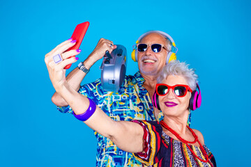 Couple of senior man and woman on blue background taking selfie - Grandpa and grandma live streaming isolated with stereo