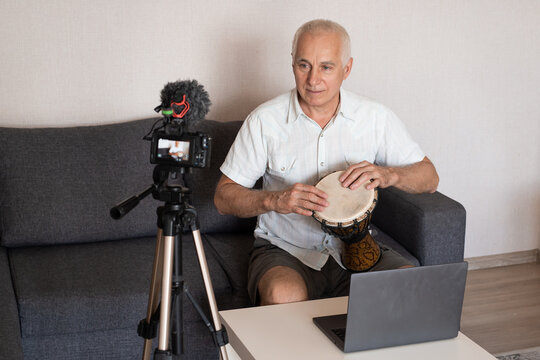 Talented Senior Man Plays Drum, Reading from a Laptop, Doing Online Video Blogging. Man Practicing Drum Music Playing at Home.