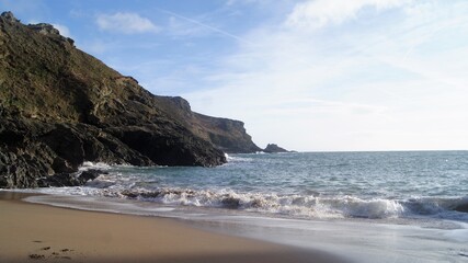 sandy beach with breaking waves under steep cliffs with blue sky and clouds SONY DSC