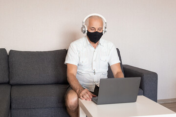 Happy elderly man in mask sitting at workplace at home indoors