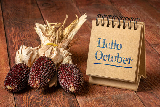 Hello October welcome note  - handwriting in a spiral sketchbook on a rustic wooden table with decorative strawberry corn, season and calendar concept