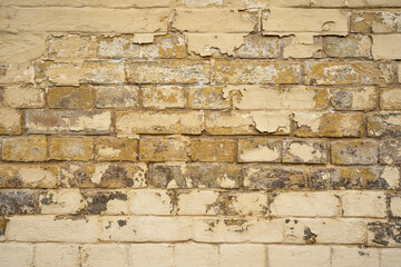 A crumbling yellow old wall. Showing expozed bricksand neglected plaster work. Most of the brickwork in yellow color, Background..