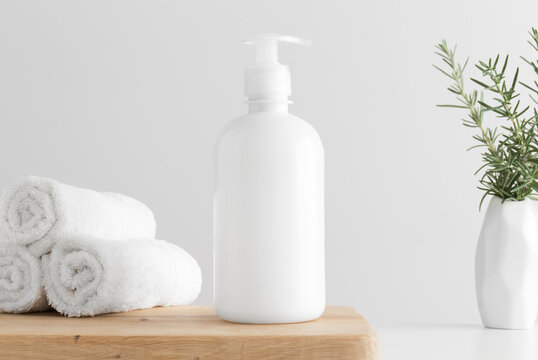 White cosmetic liquid soap dispenser bottle mockup with towels and a rosemary on a wooden table.