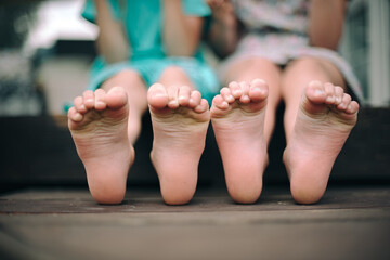 Two little girls are sitting on the terrace with their bare feet dangling. Carefree childhood.