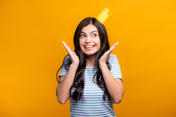 brunette woman in paper crown smiling and looking away isolated on yellow