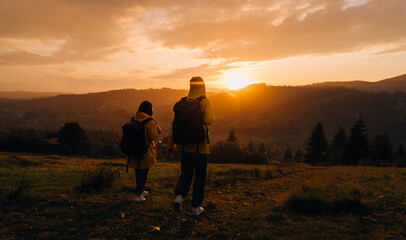 Two hikers in yellow raincoats descend from the mountain down on the background of a beautiful mountain landscape at sunset in the rain. Hikers go in rainy weather in the mountains at sunset