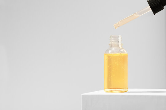 The product is a moisturizing serum for the care of female skin on a white stand. Orange essential oil dripping from a pipette into a glass bottle. Beauty concept cosmetics for skincare. Copy space