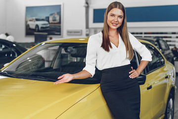 Attractive young female car dealer standing in showroom