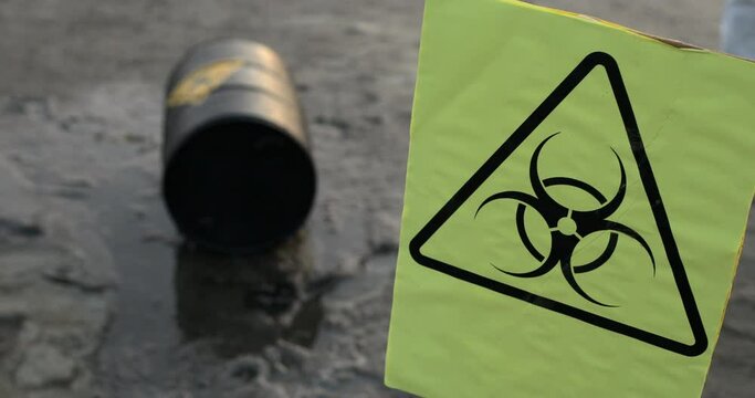 A biohazard warning sign with a black barrel lying on the ground in liquid out of focus.