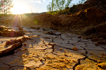 A view of a natural mosaic formed by cracks in dry clay soil in the orange slanting rays of the setting sun. Dead nature. Drought. Background and texture. Copy space.