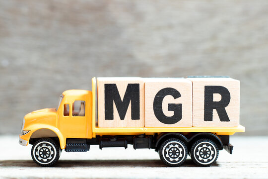 Truck hold letter block in word mgr (abbreviation of manager) on wood background