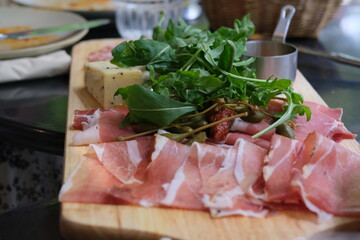 close up arugula, cured meats and cheese on wooden plate. Traditional Italian food. Defocused background