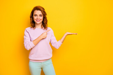 Photo of positive sales manager lady hold novelty indicating finger product on open arm advising low prices shopping wear pink sweater green pants isolated yellow color background