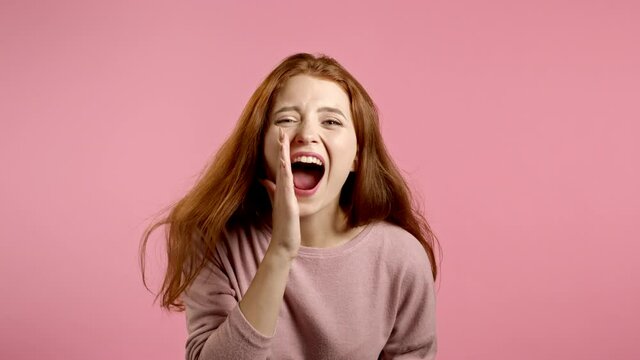Girl with red hair very glad, she screaming loud. Woman trying to get attention. Concept of sales, profitable offer. Excited happy lady on pink studio background.