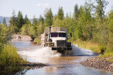 Lorry - a fuel tanker overcomes a water obstacle in a mountainous wooded area. The water level in...