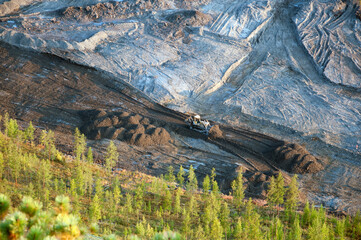  bulldozer clears an area in a mountainous woodland with an industrial bucket. View from the mountain to the construction site.