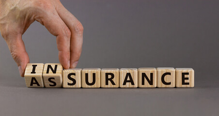 Male hand turns a cube and changes the word assurance to insurance. Beautiful grey background. Business concept. Copy space.