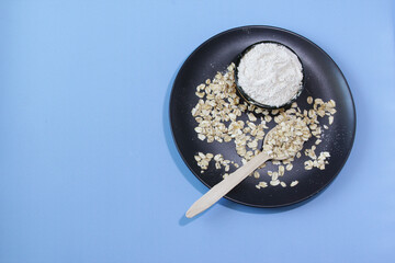 Organic uncooked oatmeal grains on plate, oat flour in bowl, blue background. Healthy concept. Top view. Copy space.