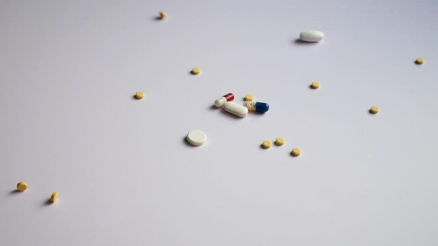 A hand pours different pills and capsules onto a white surface