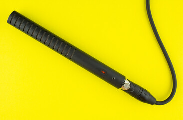 Professional instrumental condenser microphone with cable on yellow background.