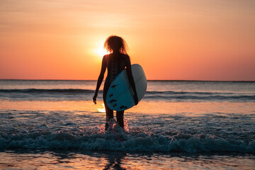 Fototapeta na wymiar Portrait of woman surfer with beautiful body on the beach with surfboard at colorful sunset.