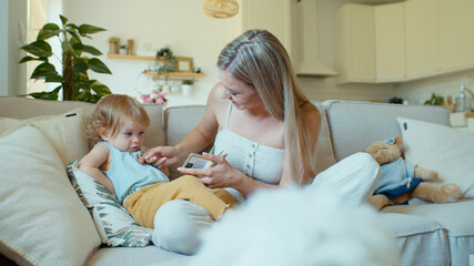 Young beautiful mother playing with baby daughter on sofa at home.