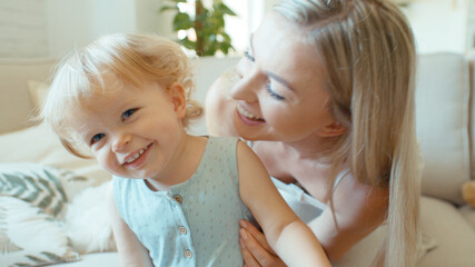 Young beautiful mother playing with baby daughter on sofa at home.