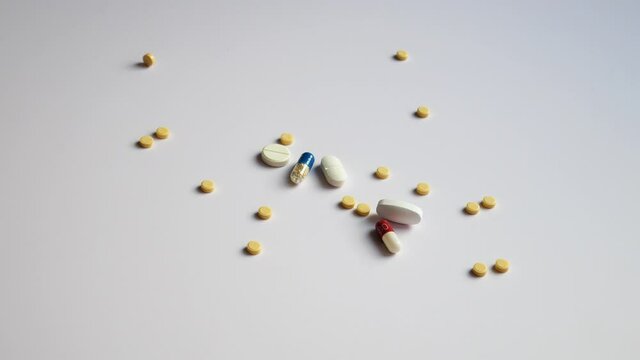 Many different pills and capsules pouring onto a white surface
