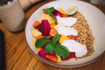 Cropped image of baked sweet granola in white plate with chopped fresh fruits for morning breakfast meal, top view of tasty sweet brunch food with homemade for healthy nutrition