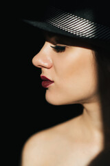 fashion portrait in profile of a young sexy girl in a black hat with red lipstick