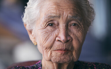 Asian old or elderly woman sitting alone smiling, wrinkled skin, white hair looking at camera,...