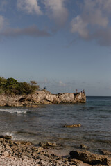 A few people, including one with a surfboard, stand in front of the sea on top of a rock formation