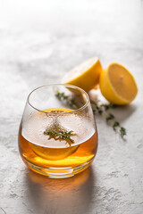 Hot tea in a glass with lemon and thyme on a gray background with copy space, side light. Autumn and winter traditional drinks.