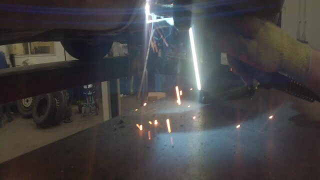Mechanic in welding mask repairing car metalwork as hot flying bright sparks fall closeup